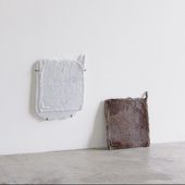 2 white and brown fabric squares leaning against a white wall, sitting on a polished concrete floor in a brightly lit room