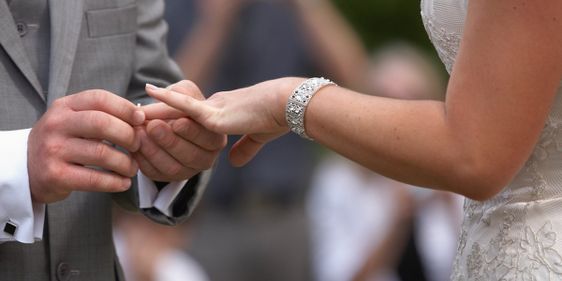 Groom placing a ring on a brides finger in the Gardens