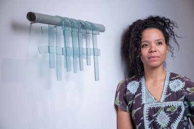 Artist Rosalind Lemoh standing next to her glass artwork.